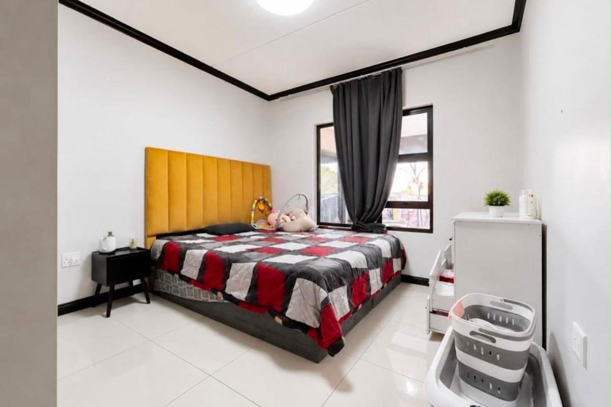 A well-maintained bedroom featuring neutral tiled flooring, a large window with dark framing, and decorative ceiling cornicing.