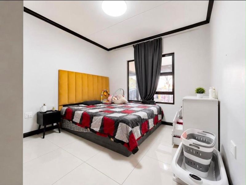 A well-maintained bedroom featuring neutral tiled flooring, a large window with dark framing, and decorative ceiling cornicing.