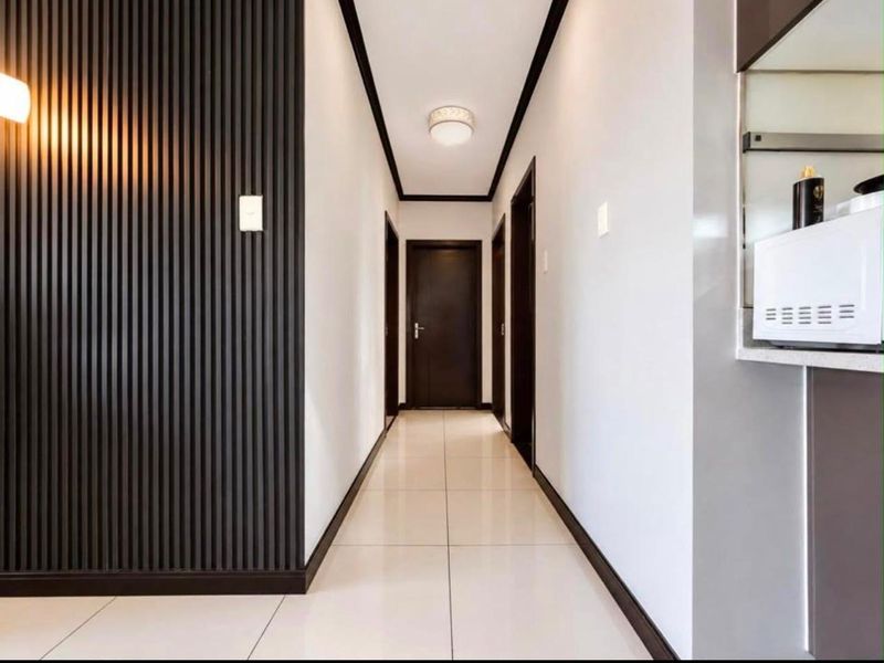 A modern, well-maintained hallway featuring sleek slatted wall paneling, neutral tiled flooring, and clean architectural lines leading to internal doors.