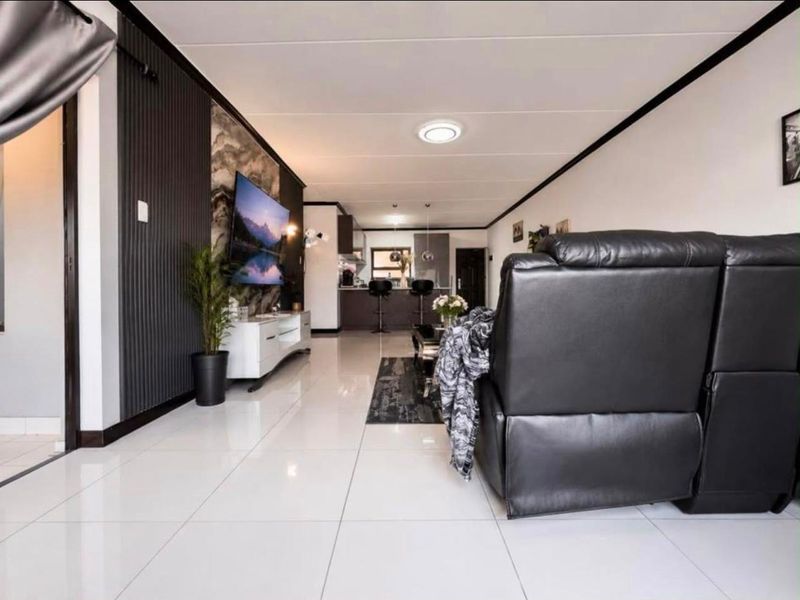 Modern open-plan living area featuring sleek tiled floors, a contemporary slatted feature wall with stone accents, and a seamless transition to the kitchen space.