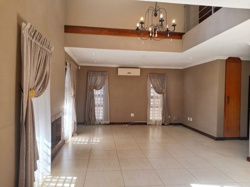 Spacious open-plan living area featuring tiled floors, a built-in fireplace, air conditioning, and a mezzanine level with a decorative chandelier.