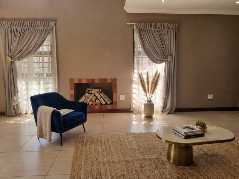 A well-lit living room featuring tiled flooring, a built-in fireplace, and large windows with elegant drapery, creating a warm and inviting atmosphere.
