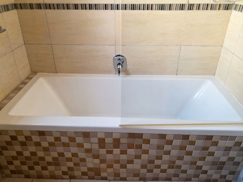 A clean bathroom featuring a built-in bathtub with a glass shower screen, chrome mixer tap, and decorative mosaic tile detailing.