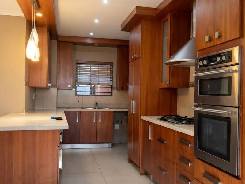 A well-maintained kitchen featuring warm wood cabinetry, stone countertops, integrated stainless steel appliances, and modern recessed lighting.