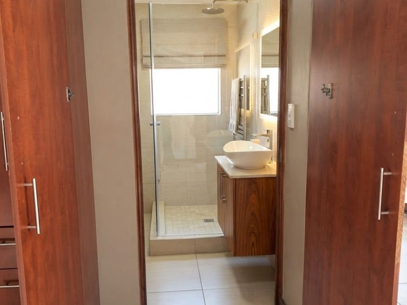 A modern bathroom featuring a walk-in shower with glass enclosure, a floating vanity with a vessel sink, and ample built-in storage cabinetry.