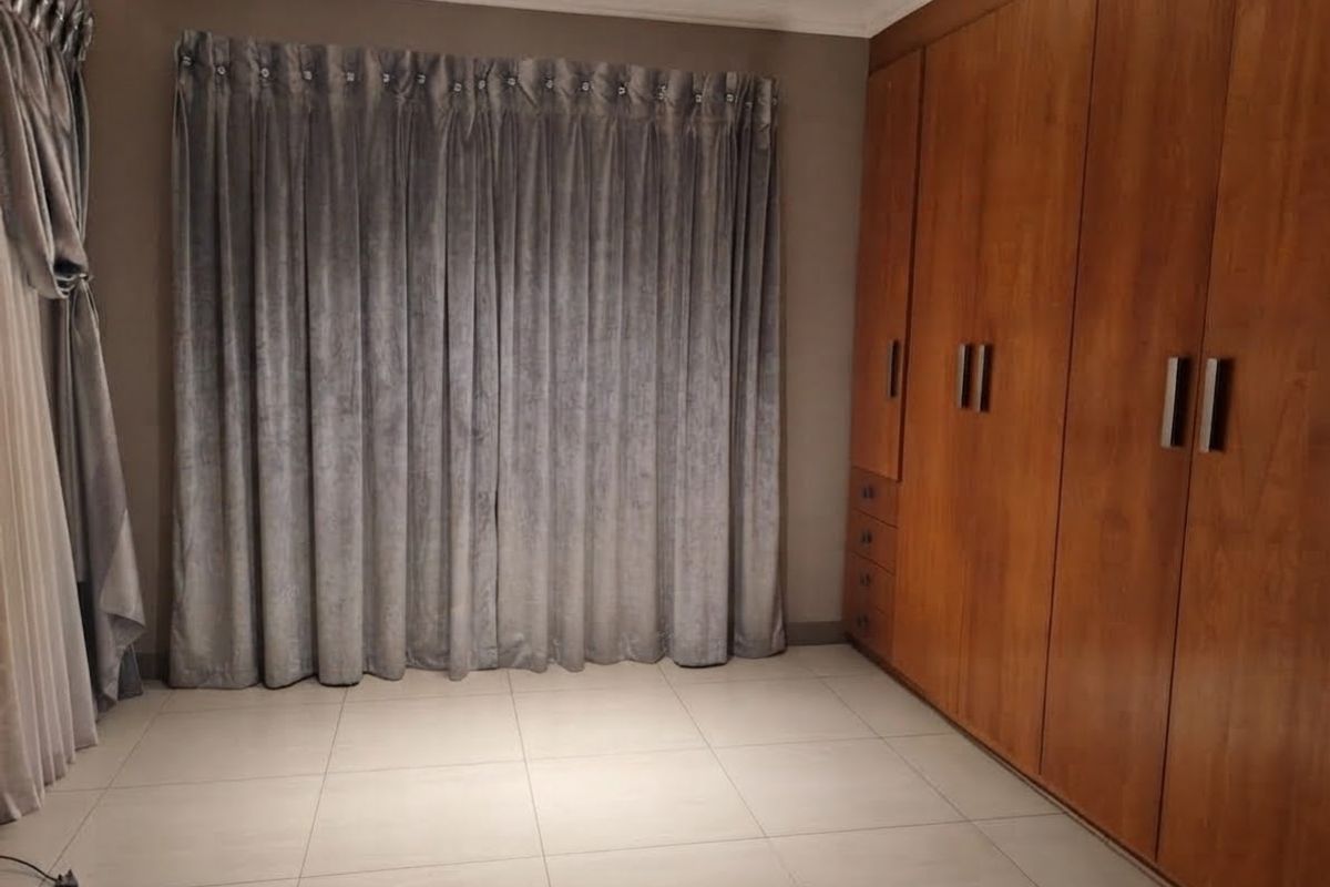 A spacious bedroom featuring neutral tiled flooring, extensive built-in wooden cabinetry, and floor-to-ceiling curtains.