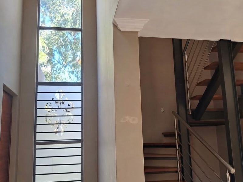 Double-volume entrance hall featuring a striking crystal chandelier, tall vertical window, and a modern steel staircase with timber treads and stainless steel balustrades.