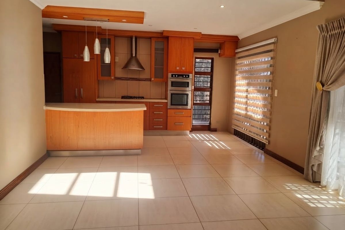 A well-maintained kitchen featuring warm-toned wooden cabinetry, built-in appliances, a breakfast counter, and large floor tiles, offering a functional and inviting culinary space.