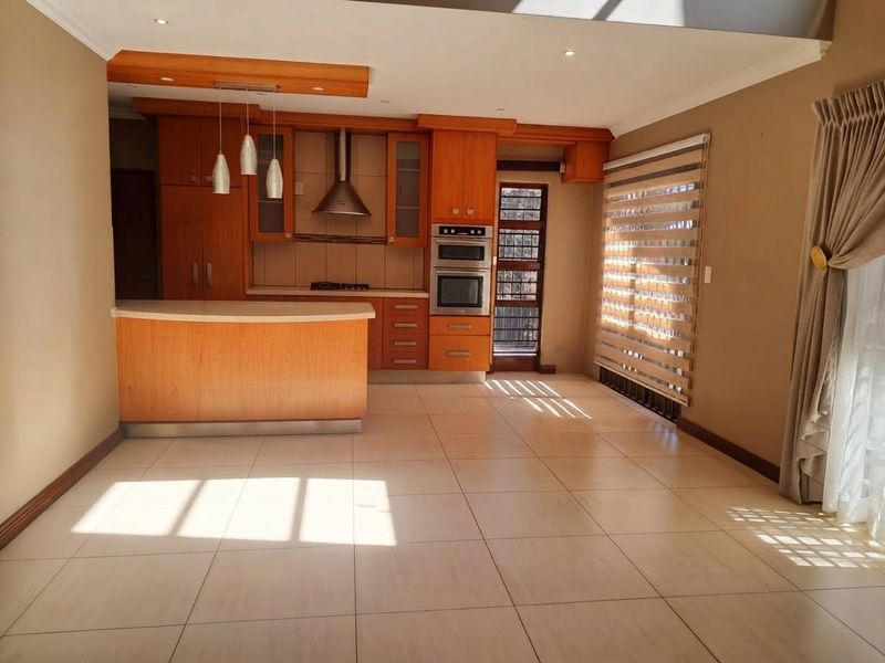 A well-maintained kitchen featuring warm-toned wooden cabinetry, built-in appliances, a breakfast counter, and large floor tiles, offering a functional and inviting culinary space.