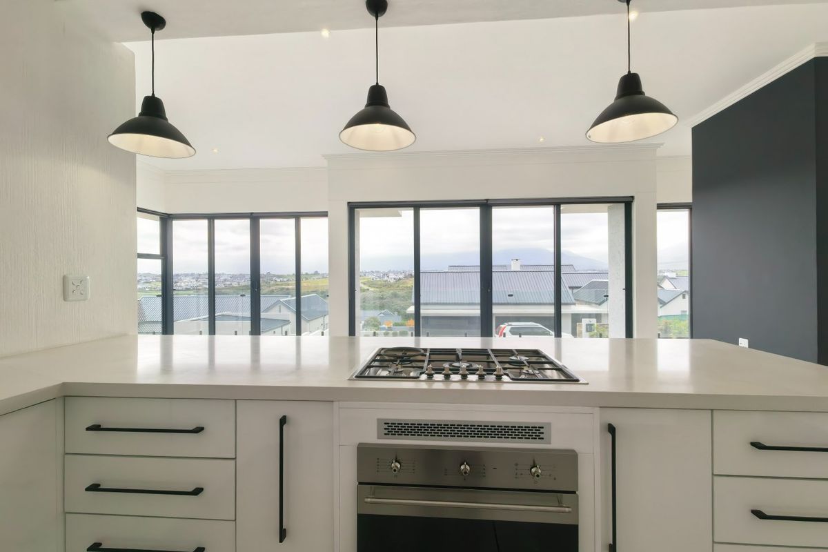 Modern kitchen featuring a central island with a built-in gas cooktop, oven, stone countertops, and large windows offering expansive views.
