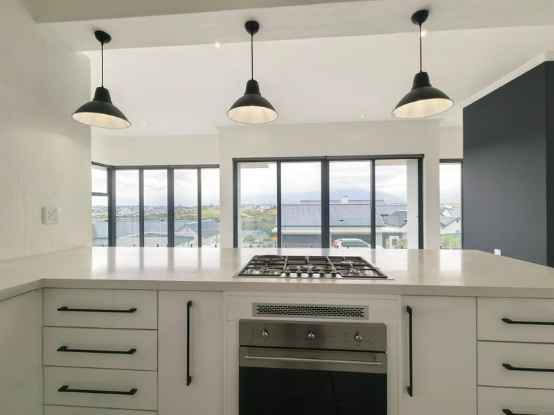 Modern kitchen featuring a central island with a built-in gas cooktop, oven, stone countertops, and large windows offering expansive views.