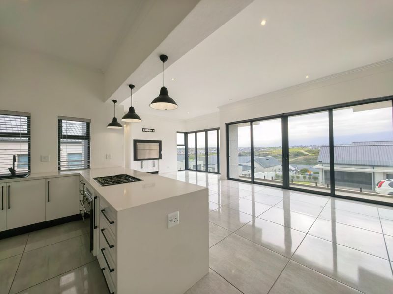 Modern open-plan kitchen and living area featuring a central island, built-in appliances, sleek cabinetry, and expansive sliding doors with scenic views.