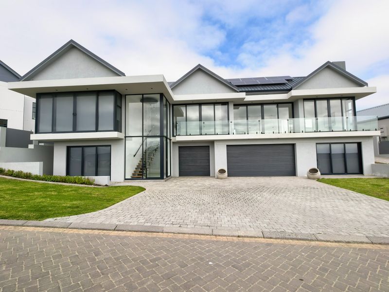 Modern double-storey residence featuring a paved driveway, double garage, expansive glass facade, and a balcony with glass balustrades.