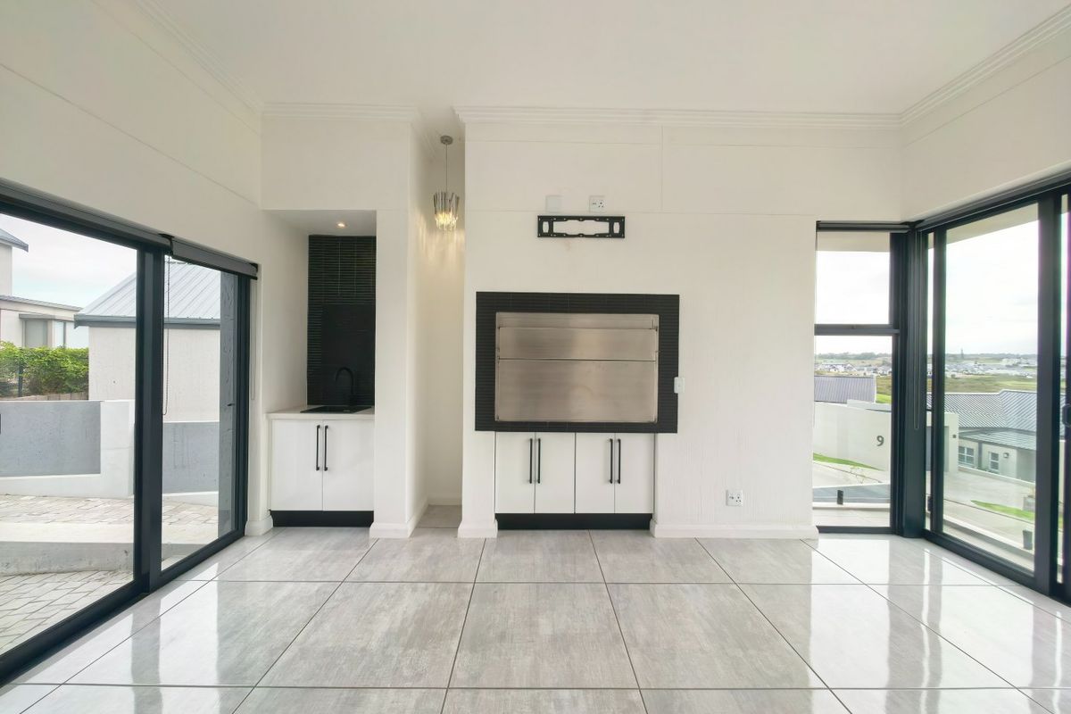 Modern living area featuring large sliding glass doors, tiled flooring, and a built-in braai with adjacent cabinetry and sink.