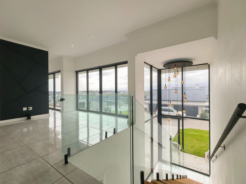 Spacious modern hallway featuring a glass balustrade, large windows with natural light, tiled flooring, and a striking feature pendant light fixture.