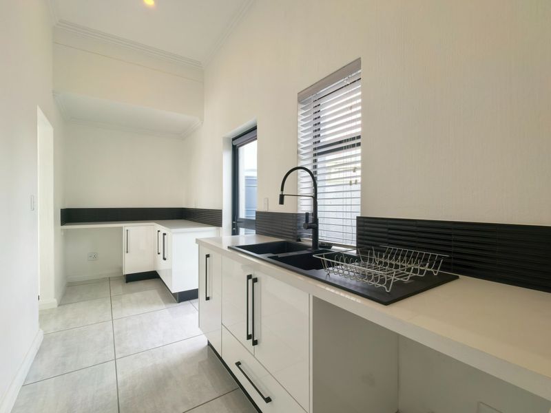 A clean, modern kitchen featuring white cabinetry, black accents, tiled backsplash, and tiled flooring with ample counter space.