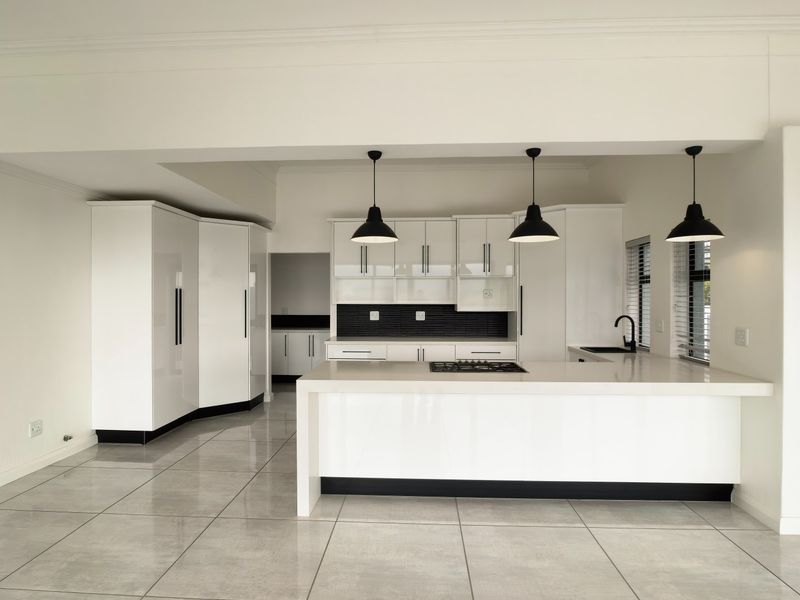 Modern, minimalist kitchen featuring white high-gloss cabinetry, a central island with a gas cooktop, sleek tiled flooring, and contemporary black pendant lighting.