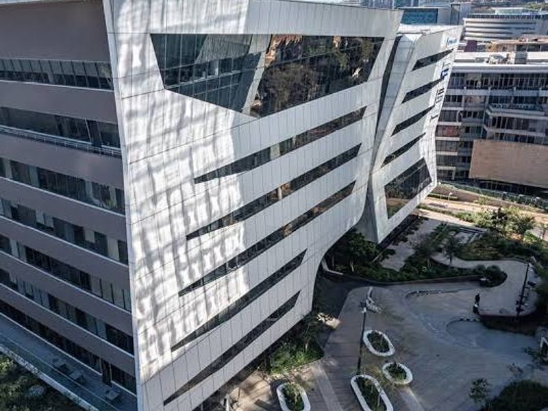 Aerial view of a modern commercial office complex featuring a striking architectural facade with extensive glass glazing and landscaped outdoor pedestrian areas.