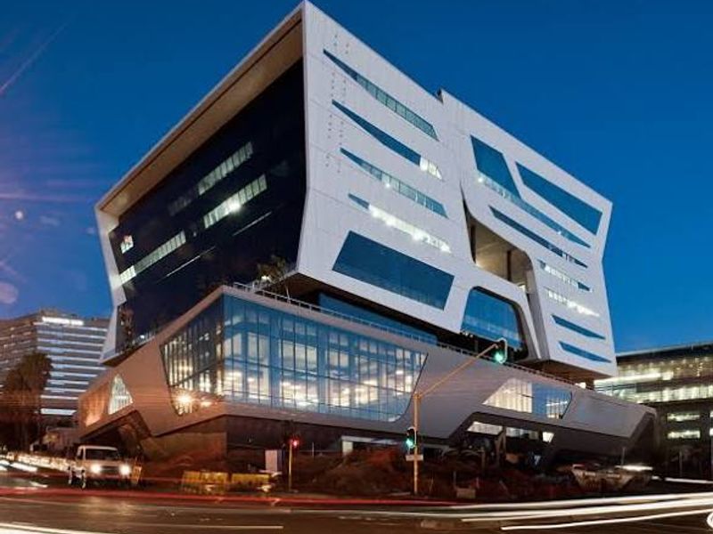 A modern, multi-story commercial office building featuring striking architectural design with extensive glass curtain walls and contemporary metal cladding at dusk.