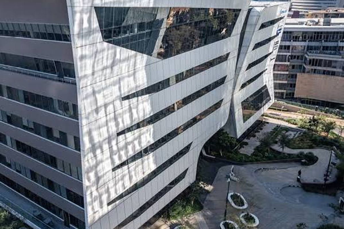 Aerial view of a modern commercial office complex featuring a striking architectural facade with extensive glass glazing and landscaped outdoor pedestrian areas.