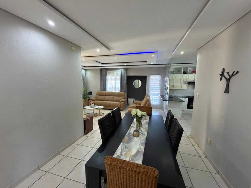 Spacious open-plan living and dining area featuring a modern tray ceiling with recessed lighting, tiled floors, and a well-appointed kitchen with granite countertops.