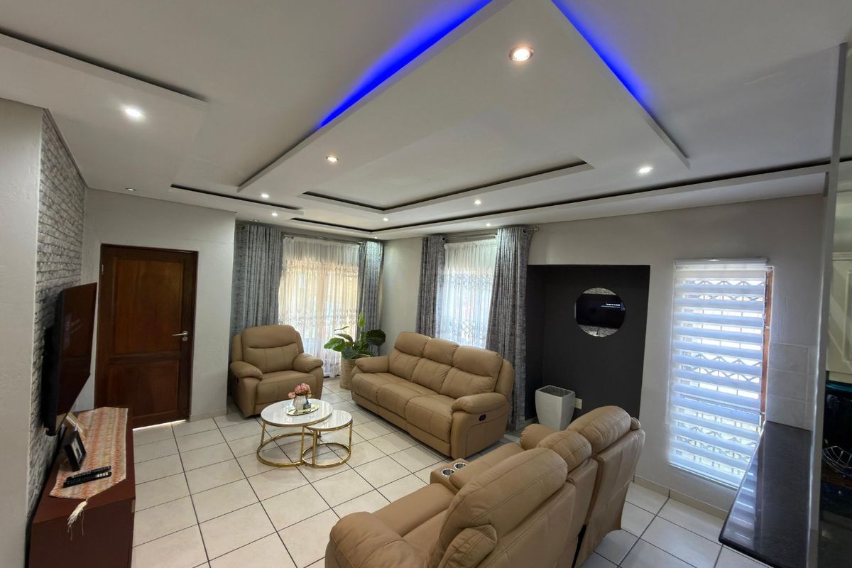A well-maintained living room featuring a modern recessed ceiling with blue LED accent lighting, tiled floors, and neutral wall finishes.