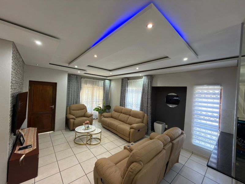 A well-maintained living room featuring a modern recessed ceiling with blue LED accent lighting, tiled floors, and neutral wall finishes.