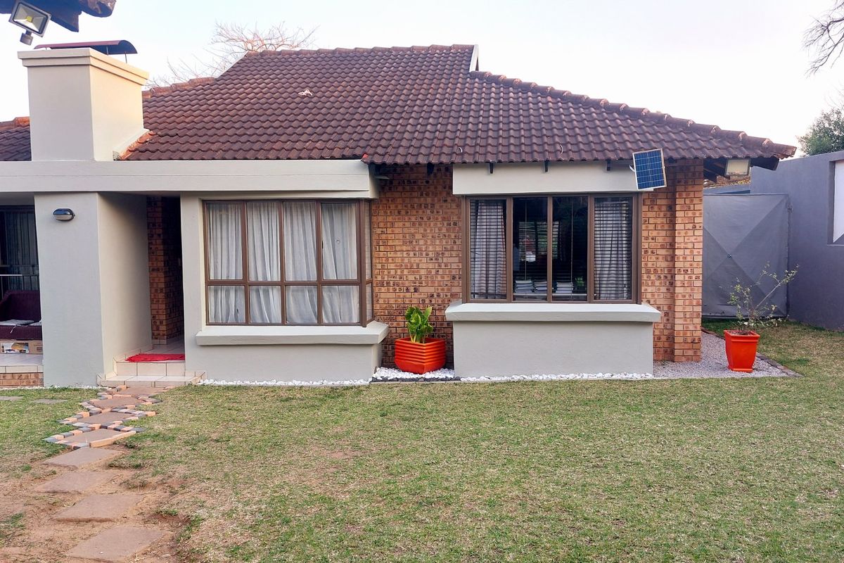A well-maintained rear exterior view of a brick house featuring a tiled roof, bay windows, and a landscaped garden area.