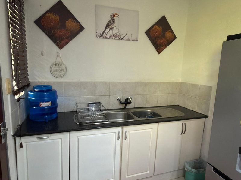 A functional scullery area featuring a double basin stainless steel sink, dark laminate countertops, and white built-in base cabinetry with tiled splashbacks.