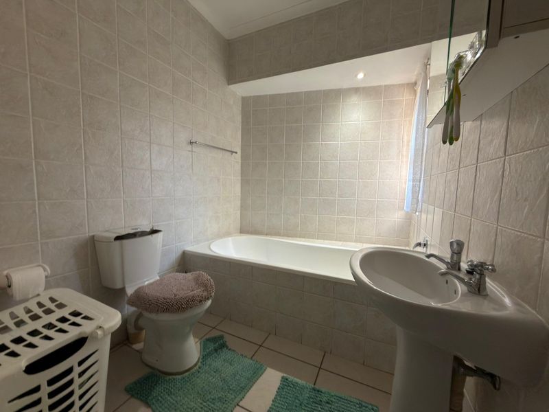 A functional bathroom featuring a pedestal basin, built-in bathtub, and toilet, finished with neutral wall and floor tiling.