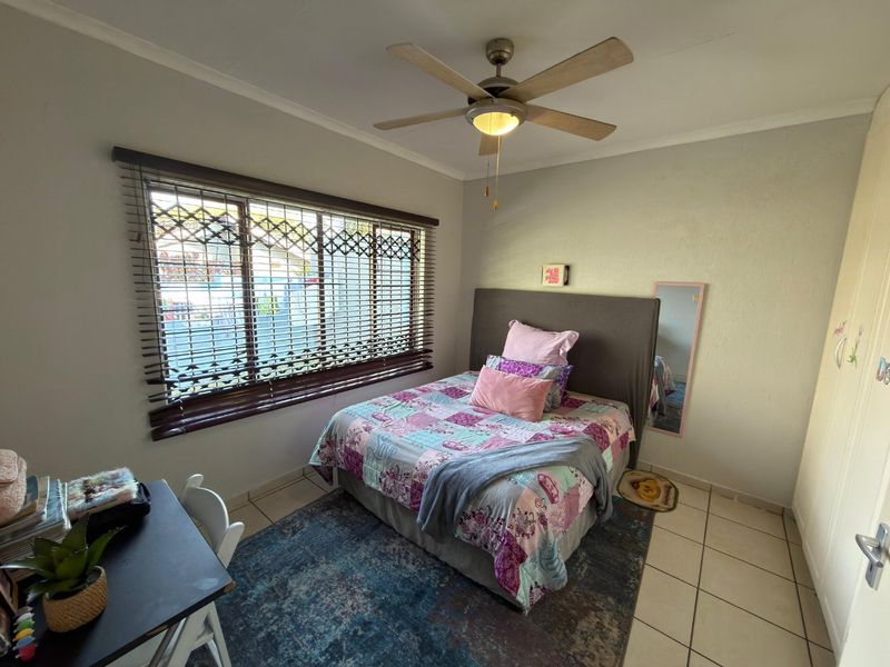A functional bedroom featuring tiled flooring, a ceiling fan, and built-in cupboards, with a security gate installed on the window.