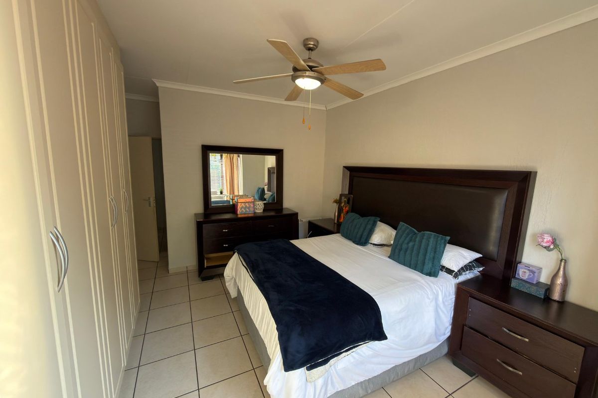 A well-maintained bedroom featuring built-in cupboards, tiled flooring, and a central ceiling fan.