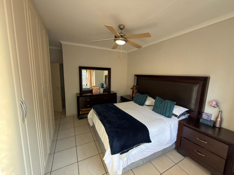 A well-maintained bedroom featuring built-in cupboards, tiled flooring, and a central ceiling fan.
