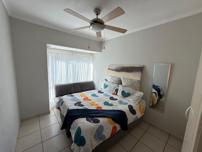 A functional bedroom featuring tiled flooring, a central ceiling fan, and a recessed window area allowing for natural light.