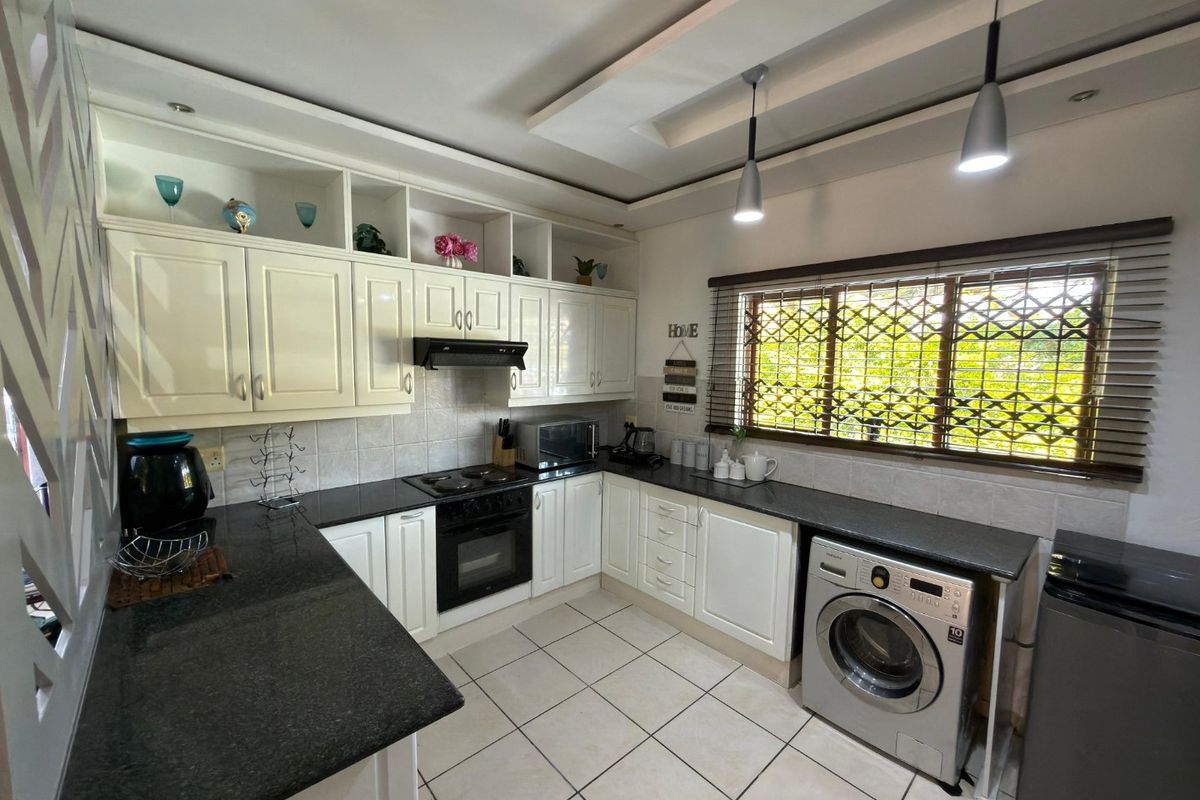 A well-maintained kitchen featuring granite countertops, built-in cabinetry, an integrated oven and hob, and tiled flooring with a functional layout.