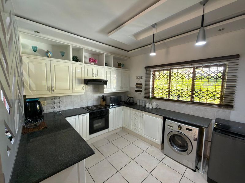 A well-maintained kitchen featuring granite countertops, built-in cabinetry, an integrated oven and hob, and tiled flooring with a functional layout.