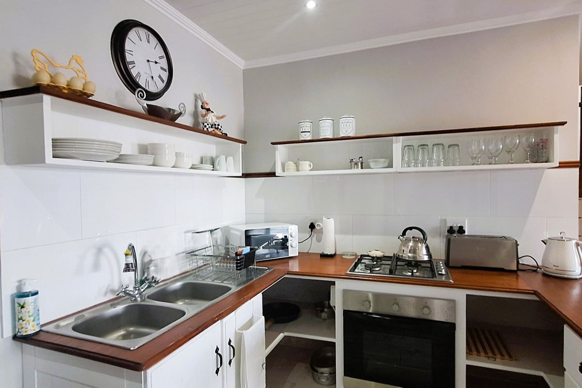 A functional kitchen featuring wooden countertops, a double basin sink, built-in oven, gas hob, and open shelving with tiled splashbacks.