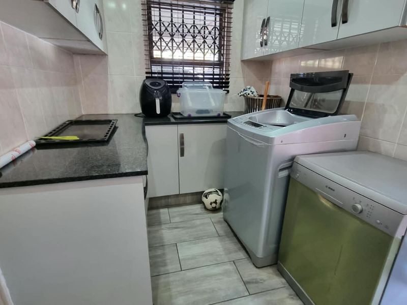 A functional laundry room featuring tiled walls, granite countertops, and built-in cabinetry with space for appliances.