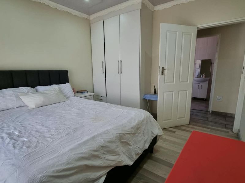 A bedroom featuring built-in cupboards, laminate flooring, and decorative cornice, with an adjoining view into a bathroom.