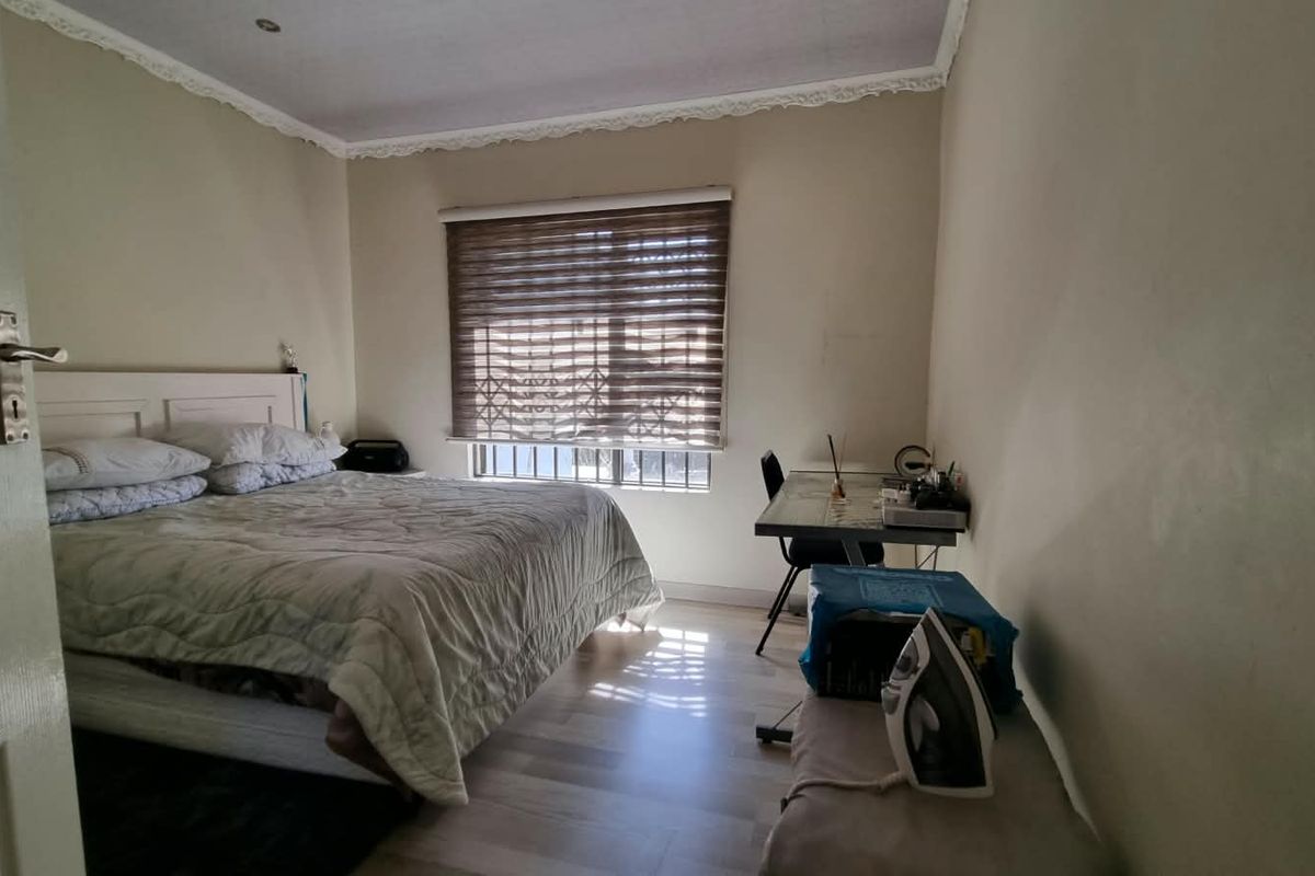 A functional bedroom featuring laminate flooring, window security bars, and decorative ceiling cornicing, offering a neutral base for personalization.