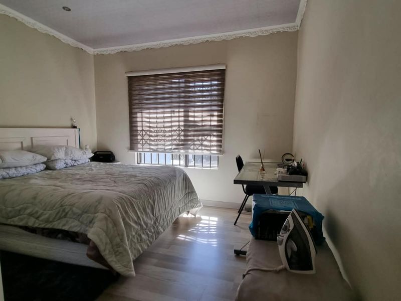 A functional bedroom featuring laminate flooring, window security bars, and decorative ceiling cornicing, offering a neutral base for personalization.