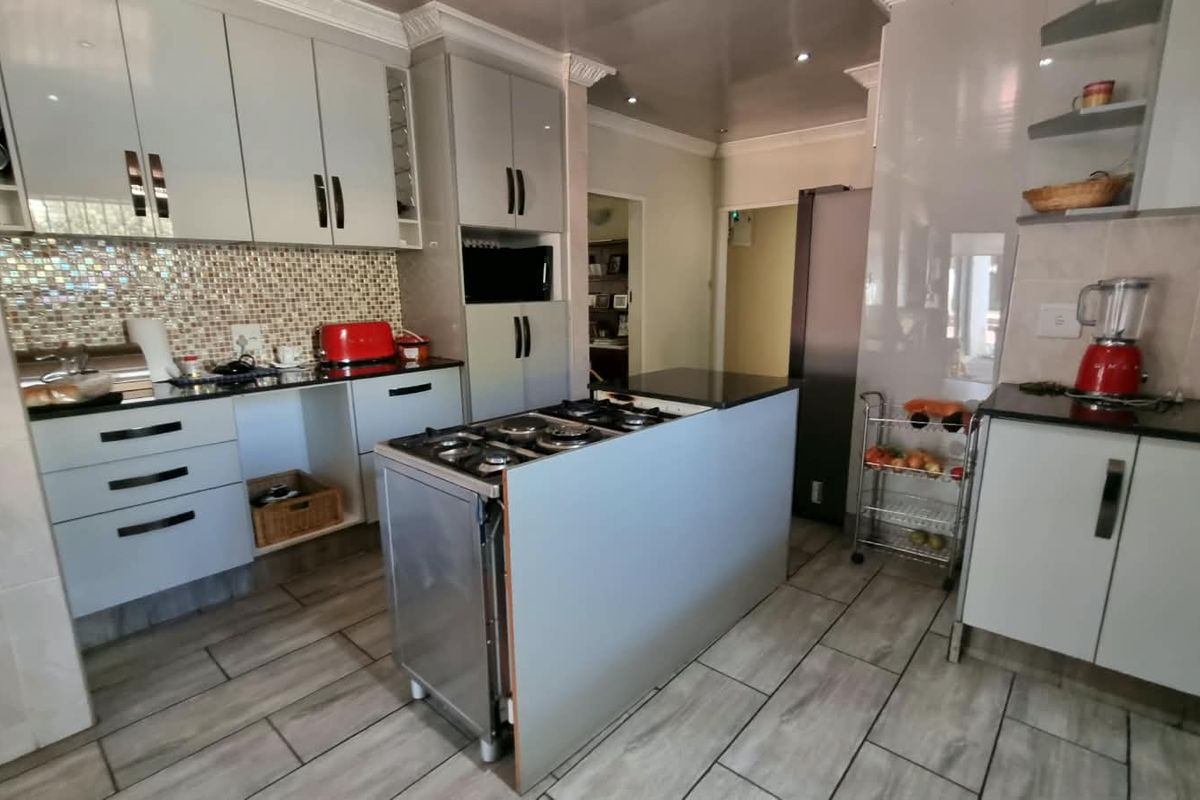 A functional kitchen featuring light-toned cabinetry, granite countertops, a mosaic tile backsplash, and a central island with an integrated gas hob.