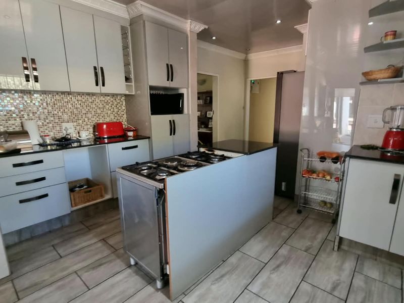 A functional kitchen featuring light-toned cabinetry, granite countertops, a mosaic tile backsplash, and a central island with an integrated gas hob.