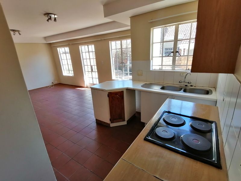Open plan kitchen and living area featuring tiled floors, built-in cabinetry, electric hob, and multiple windows providing natural light.