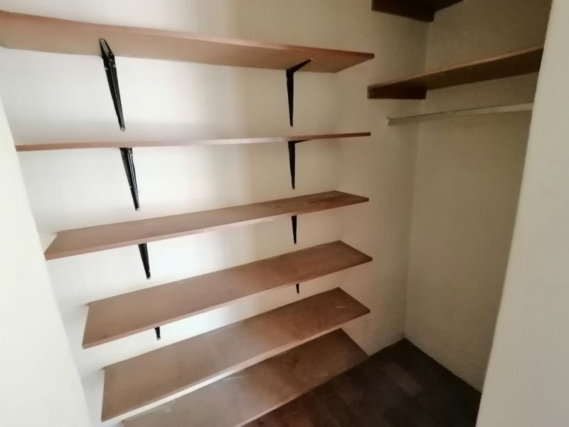 A functional storage closet or pantry area featuring multiple built-in wooden shelves and a hanging rail for organized storage.