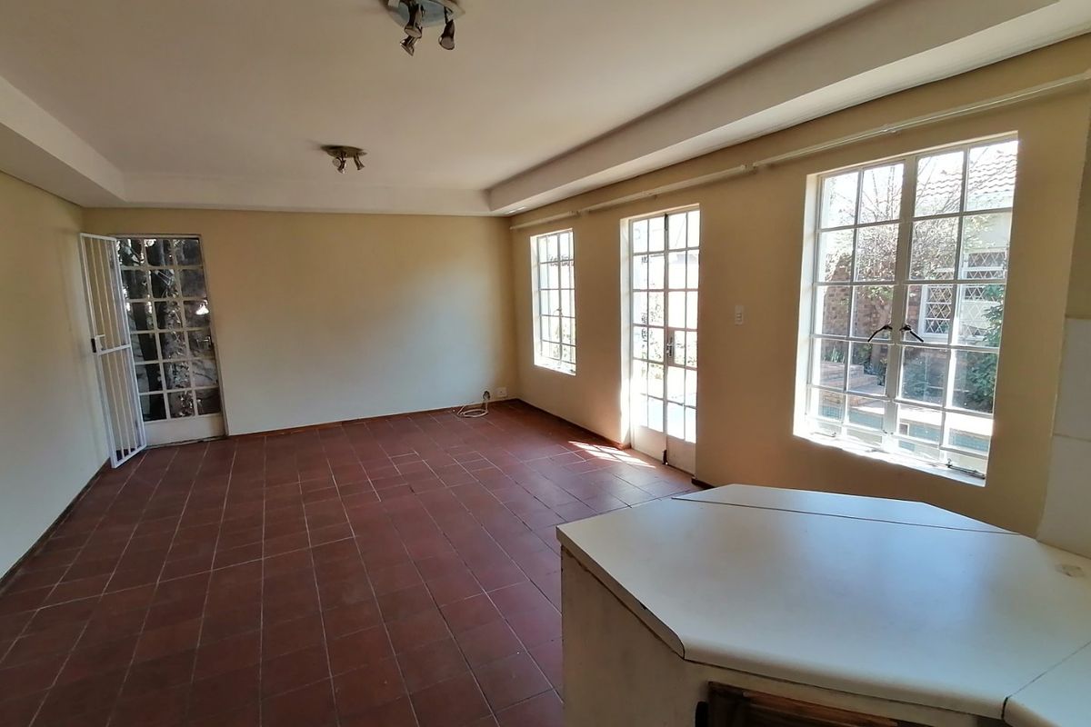 Spacious open-plan living area featuring terracotta tiled flooring, abundant natural light through multiple windows and doors, and a built-in kitchen counter.