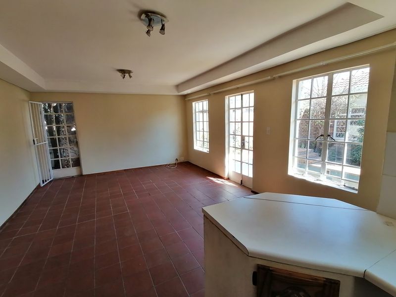 Spacious open-plan living area featuring terracotta tiled flooring, abundant natural light through multiple windows and doors, and a built-in kitchen counter.