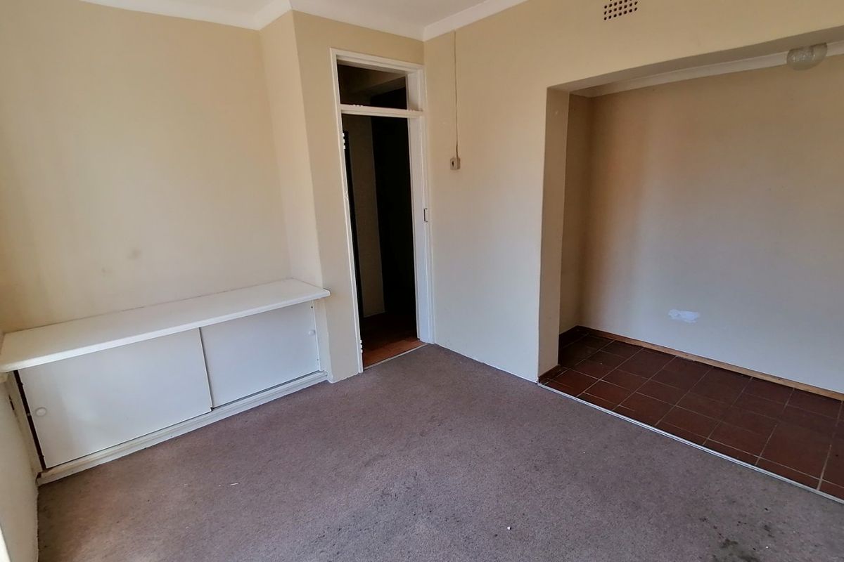 An empty living area featuring carpet flooring, built-in cabinetry, and a separate tiled alcove space, presenting a blank canvas for renovation.