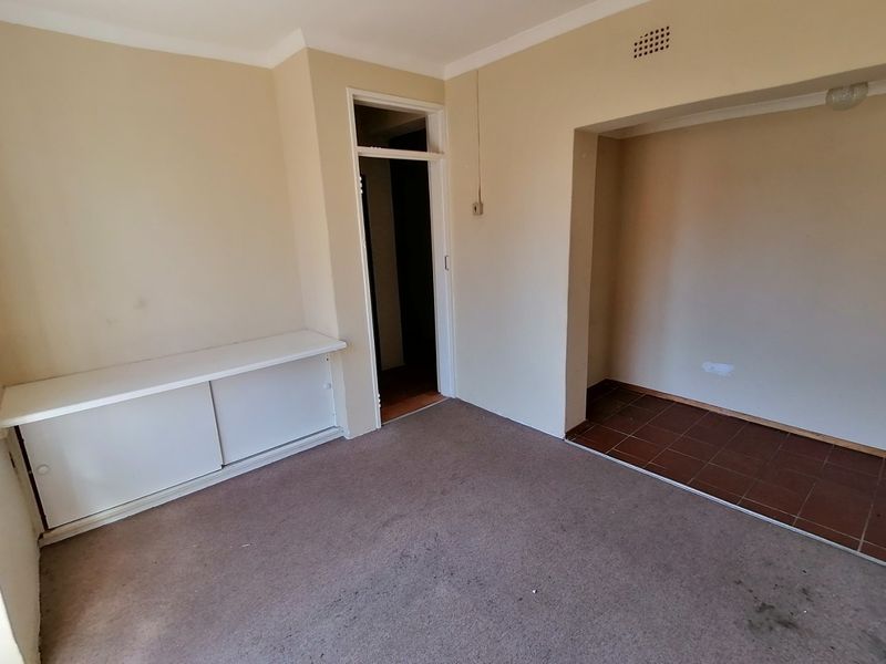 An empty living area featuring carpet flooring, built-in cabinetry, and a separate tiled alcove space, presenting a blank canvas for renovation.