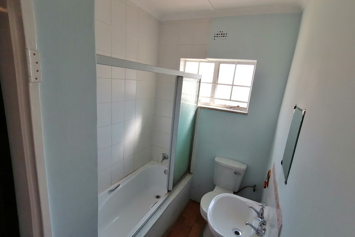 A functional bathroom featuring a bathtub with a shower screen, a pedestal basin, and a toilet, requiring cosmetic updates to modernize the space.